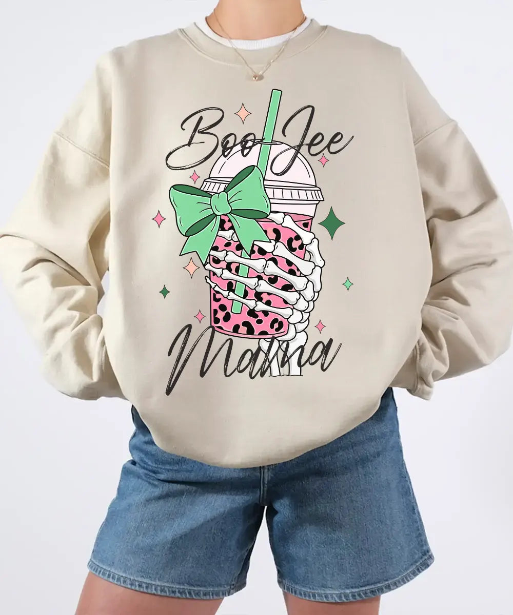 Person wearing sand crewneck sweatshirt with a graphic design of a pink drink with a straw and bow, text 'Boo Jee Mama'.