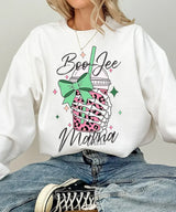 Person wearing white crewneck sweatshirt with a graphic design of a pink drink with a straw and bow, text 'Boo Jee Mama'.